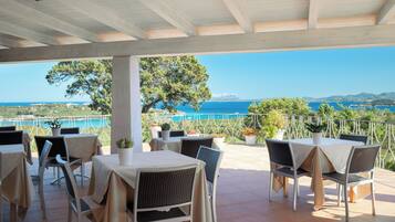 An outdoor terrace with tables and chairs, overlooking a coastal landscape.