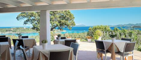 An outdoor terrace with tables and chairs, overlooking a coastal landscape.