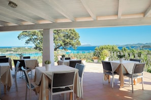 An outdoor terrace with tables and chairs, overlooking a coastal landscape. - Hotel Valdiola (Arzachena)