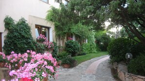 A stone pathway leading to a building with a garden. There are potted plants and flowers along the path. - Hotel Valdiola (Arzachena)