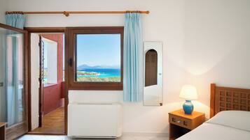 A hotel room with a view of the sea, a bed, a nightstand with a lamp, and a window with curtains.