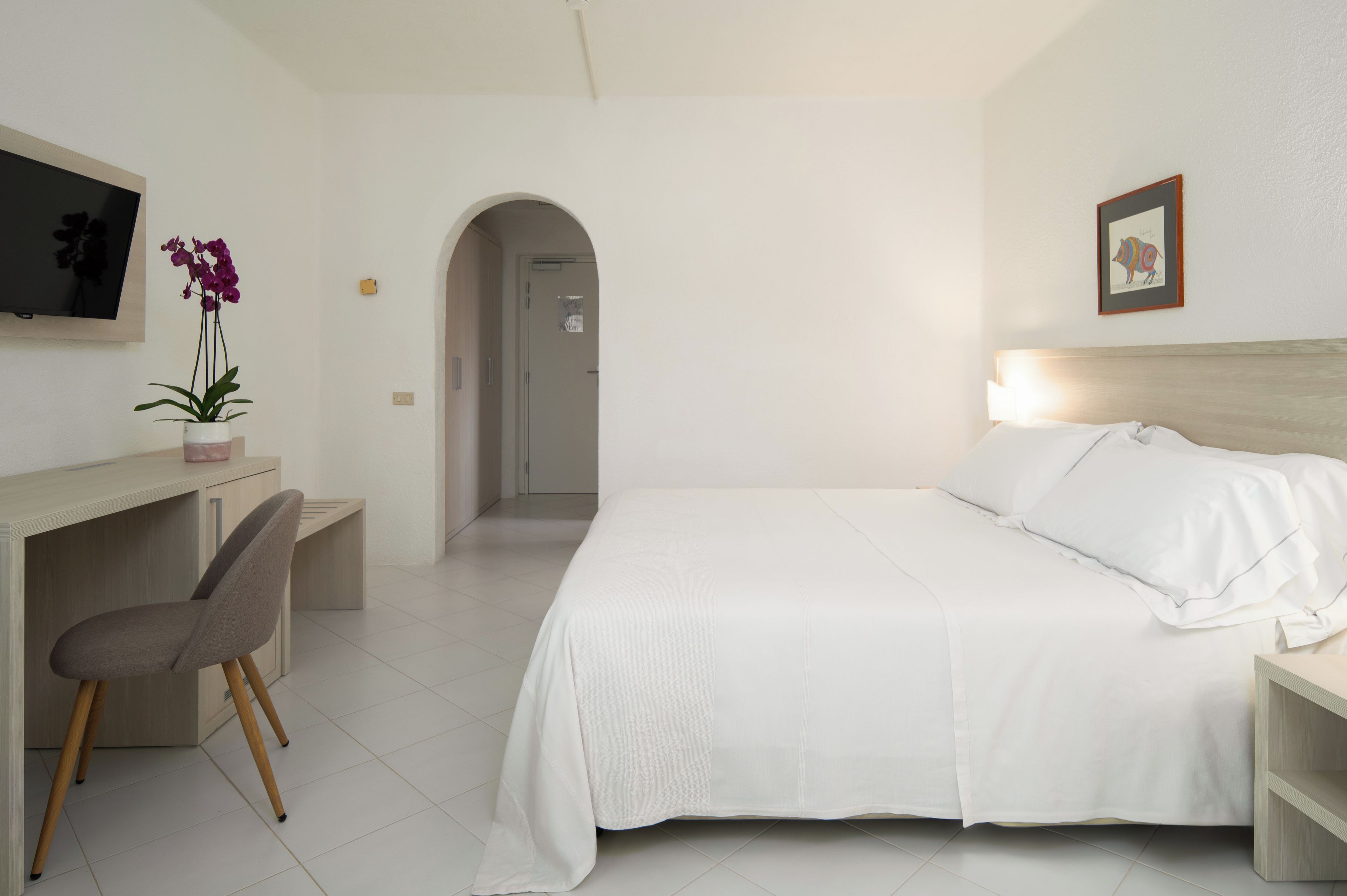 Une chambre d’hôtel équipée d’un lit, d’un bureau, d’une chaise, d’une télévision et d’une porte donnant accès à une salle de bain.