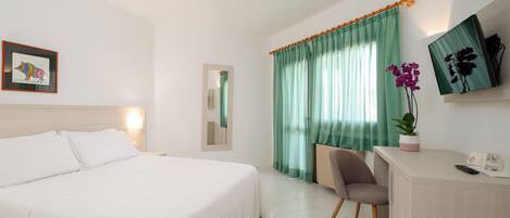 A hotel room with a bed, a desk, a chair, a television, and a window with curtains.