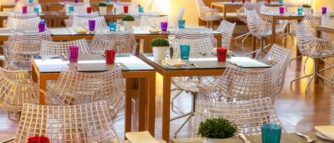 Un comedor de hotel con varias mesas y sillas, cada conjunto con un posavasos, cubiertos y una pequeña planta.