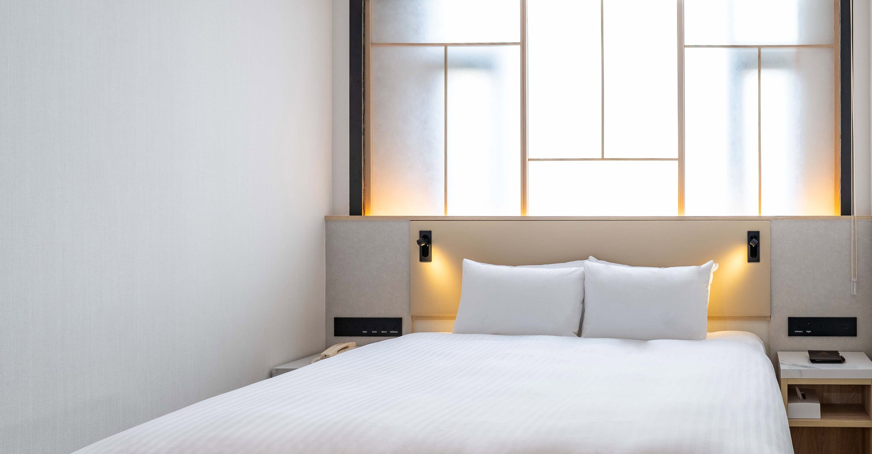A modern hotel room with a large bed, bedside tables, and a wall-mounted light fixture.