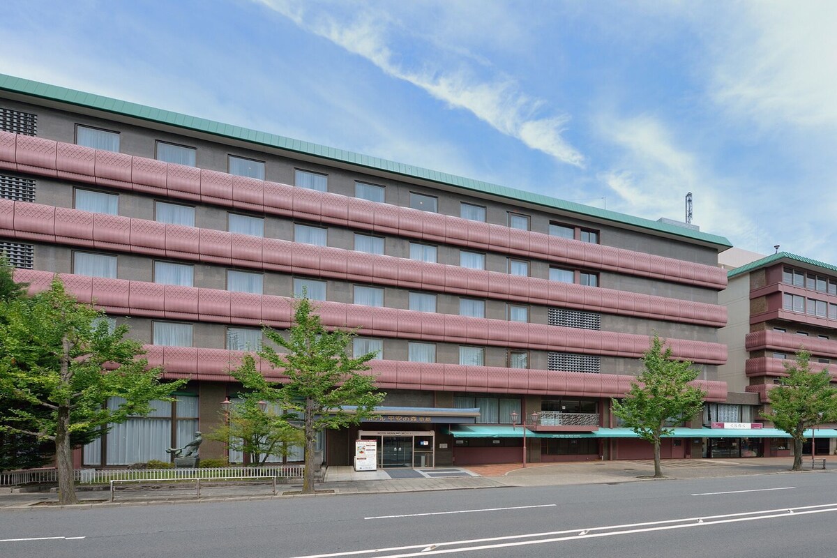 Um hotel com vários andares, com fileiras de quartos em cada andar, um telhado verde e um estacionamento em frente.
