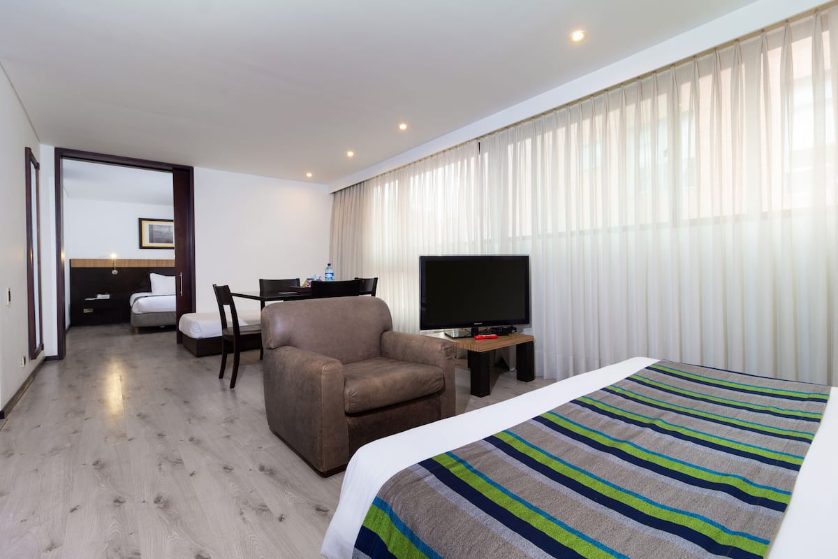 A hotel room with a bed, a TV, a chair, a desk, and a bathroom visible through an open door.