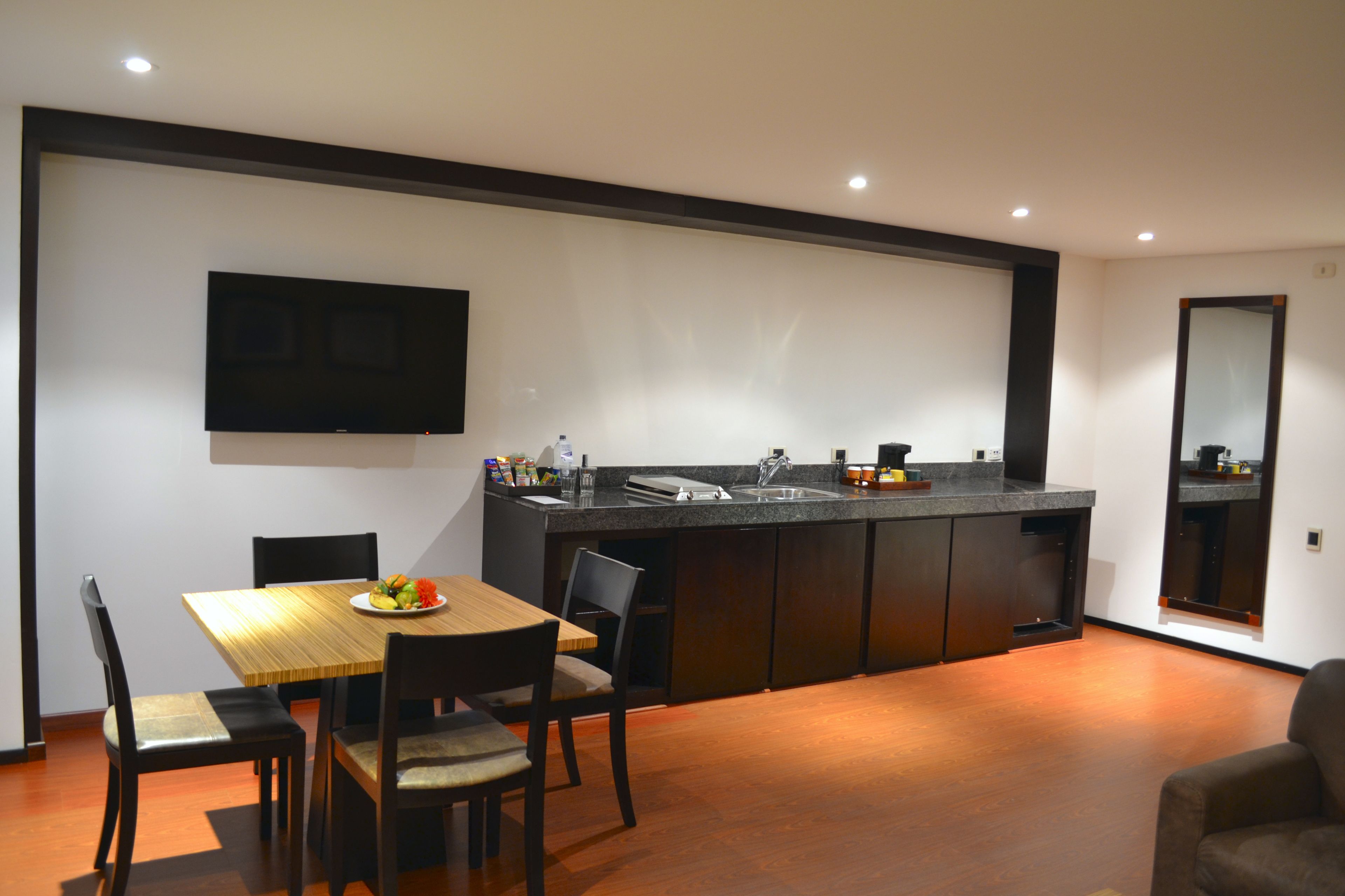 A modern kitchen with a dining area, a flat-screen TV mounted on the wall, and a large mirror on the wall.