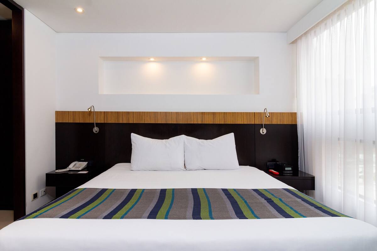 A hotel room with a bed, a nightstand, a phone, and a window with curtains.