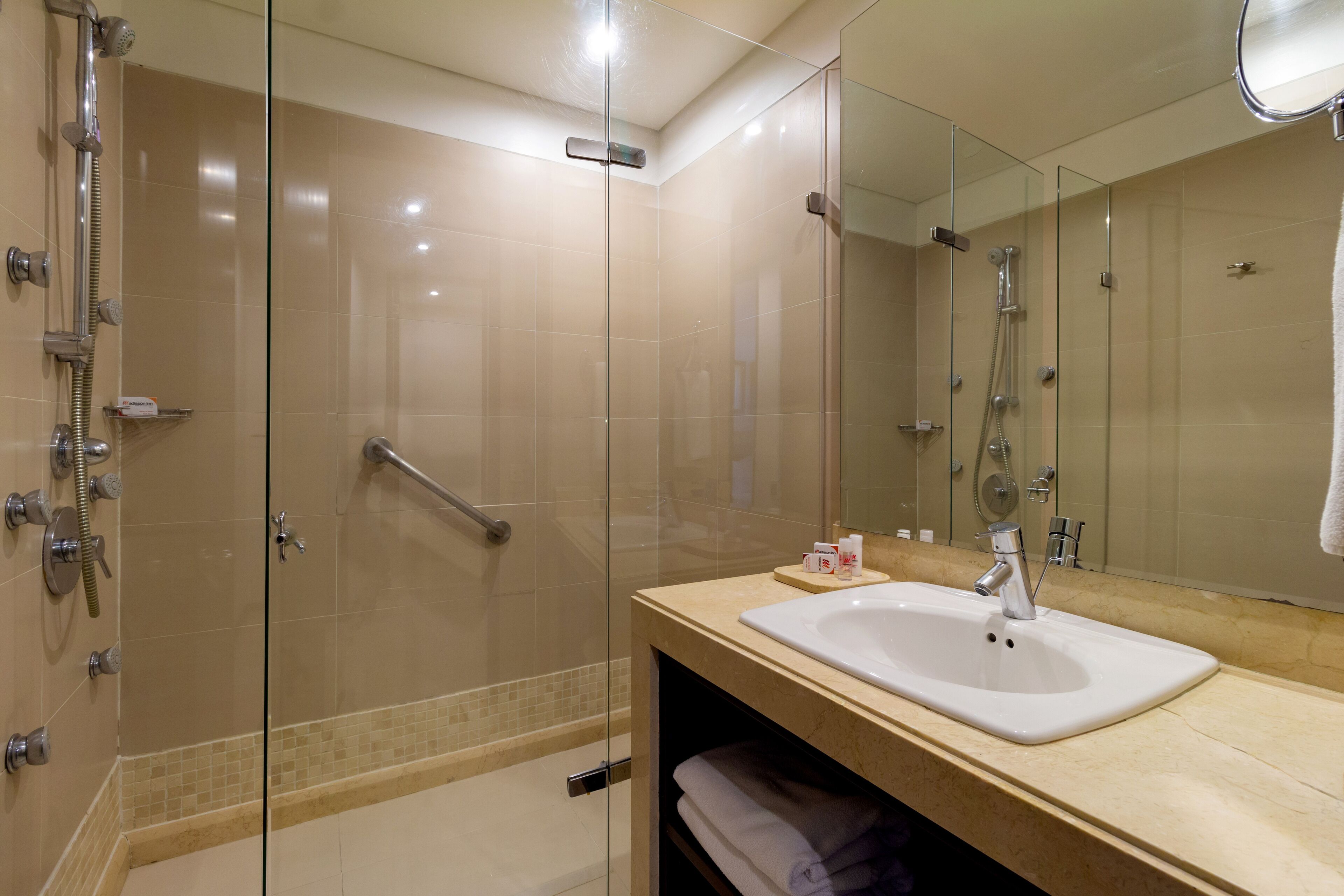 Uma casa de banho moderna com chuveiro envidraçado, lavatório com espelho e porta-toalhas.