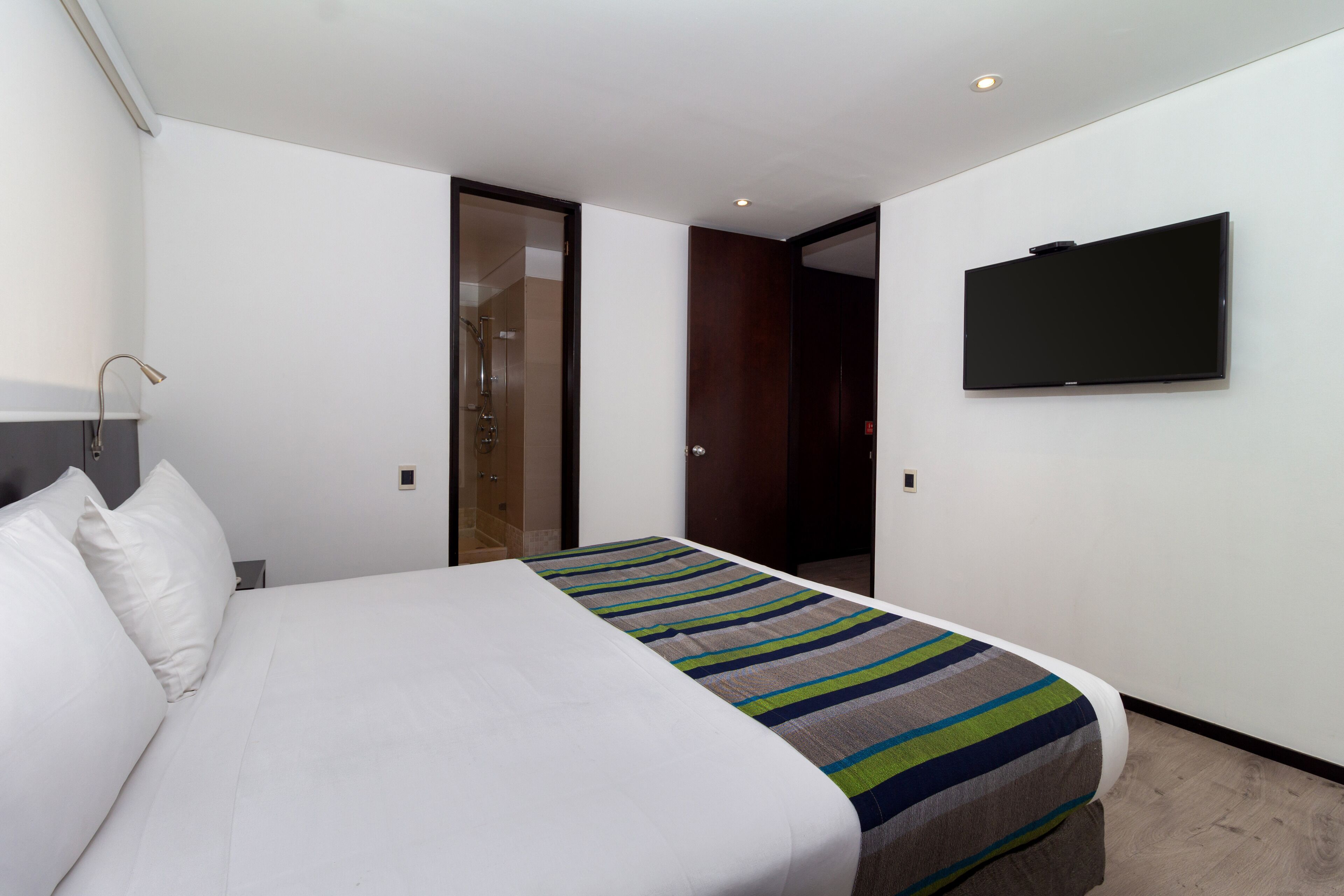 Habitación de hotel con una cama, un televisor de pantalla plana montado en la pared y una puerta que da al baño.