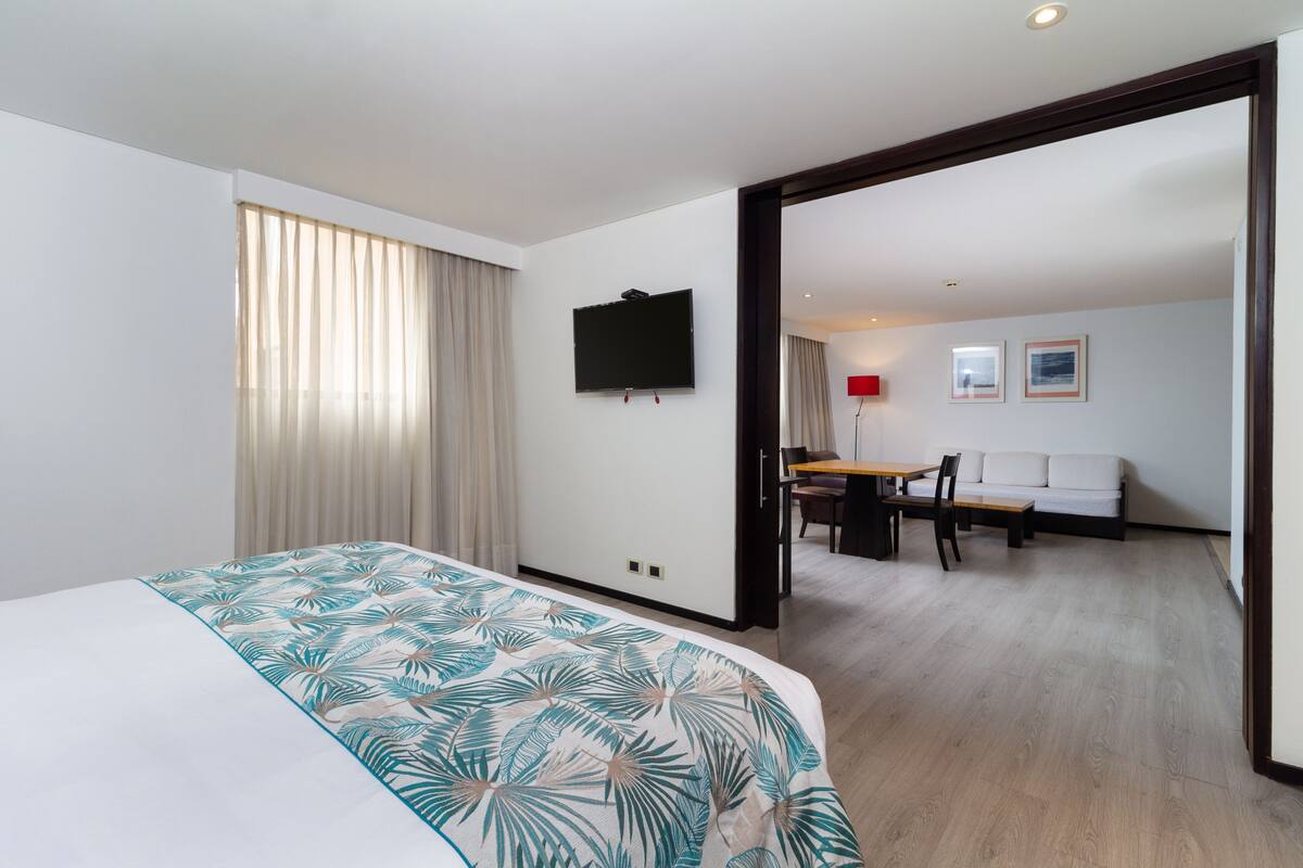 A hotel room with a bed, a television, a dining area with a table and chairs, and a sofa.