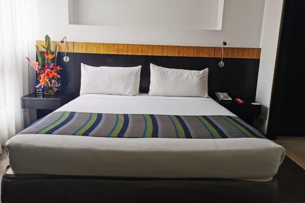 A hotel room with a bed, a nightstand, a telephone, and a wall-mounted light fixture.
