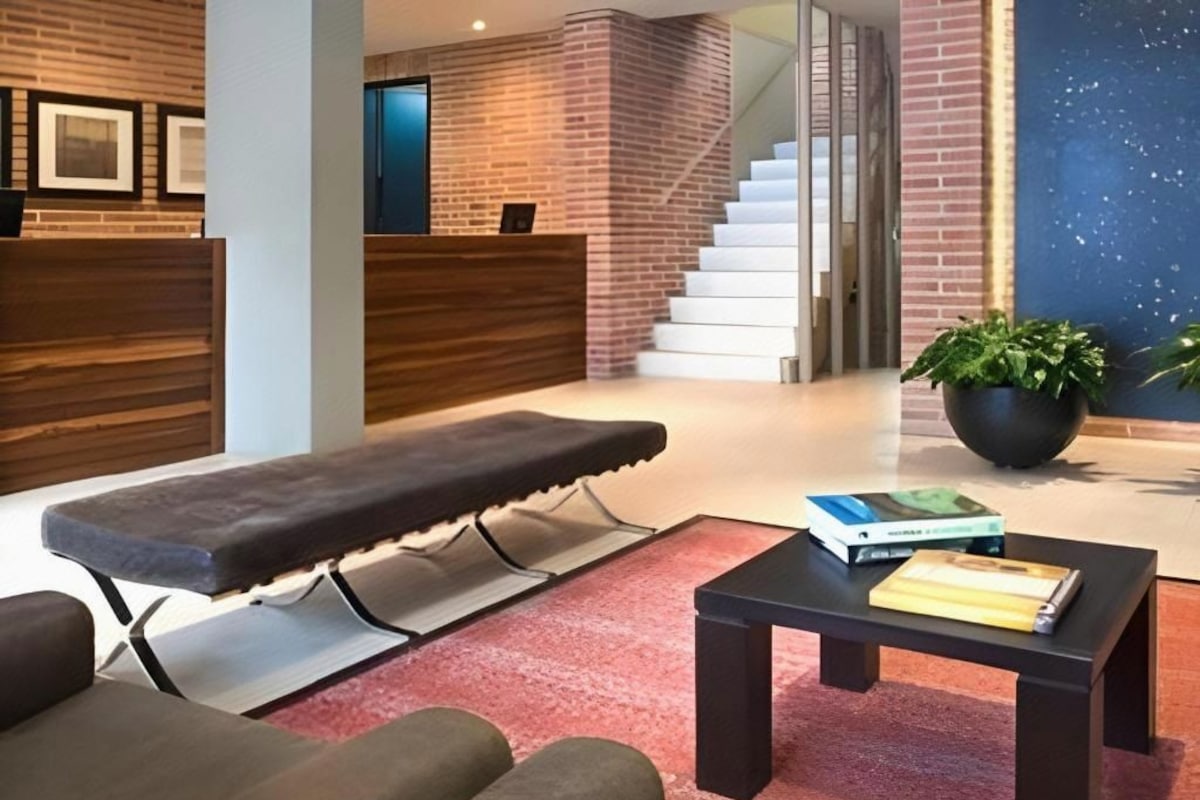 A reception area with a reception desk, a bench, a coffee table, and a staircase in the background.
