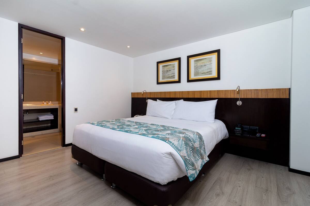 A modern hotel room with a large bed, a wooden headboard, two framed certificates on the wall, and a built-in wardrobe.