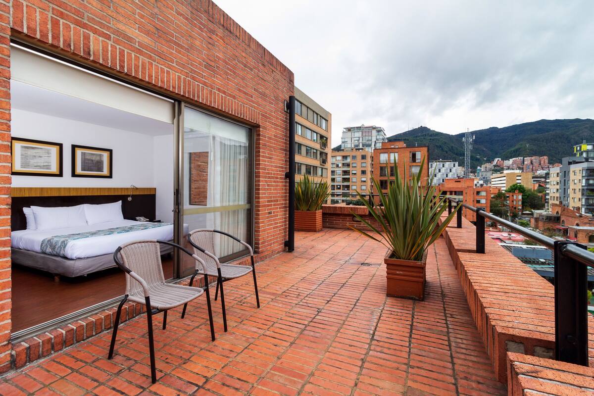 A balcony with a bed, two chairs, and potted plants.