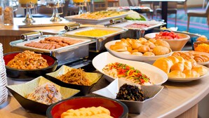 Buffet com diversas opções de comida, incluindo cachorros-quentes, saladas e doces.