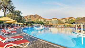 Piscina do resort com espreguiçadeiras, guarda-sóis e montanhas ao fundo.
