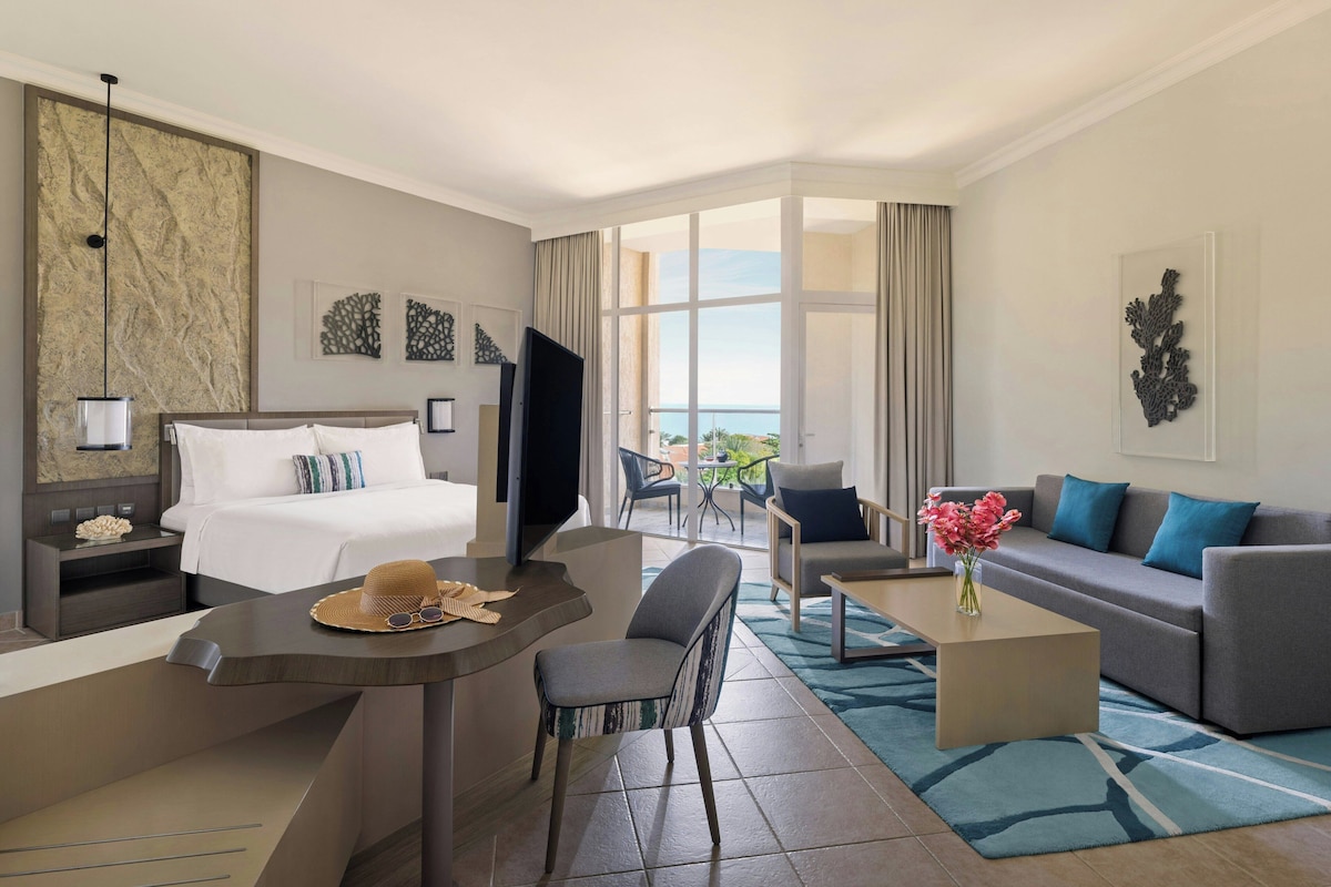 Habitación de hotel con cama, escritorio, sofá y balcón con vistas.