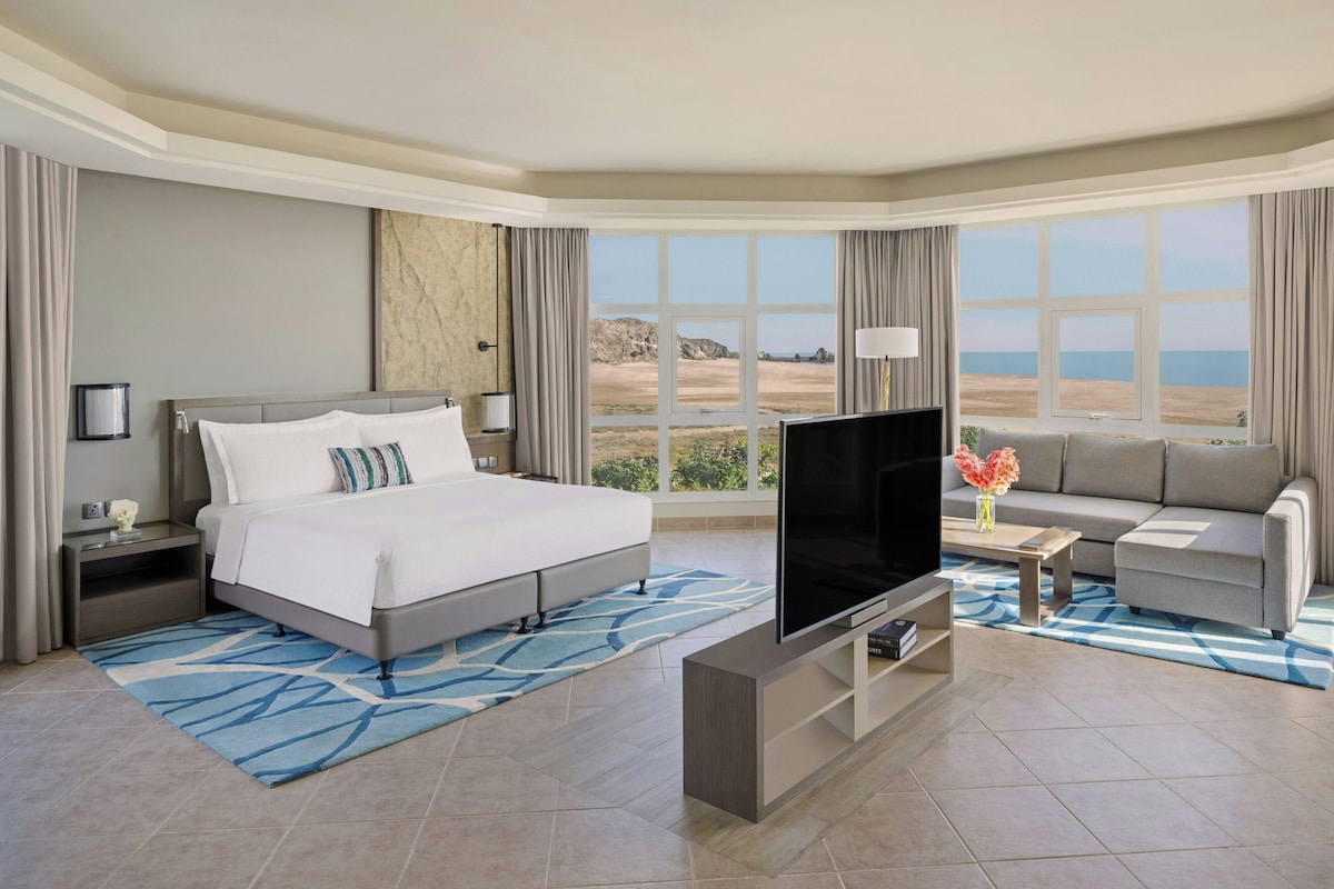 Una habitación de hotel con cama, televisor, sofá y un amplio ventanal con vistas.