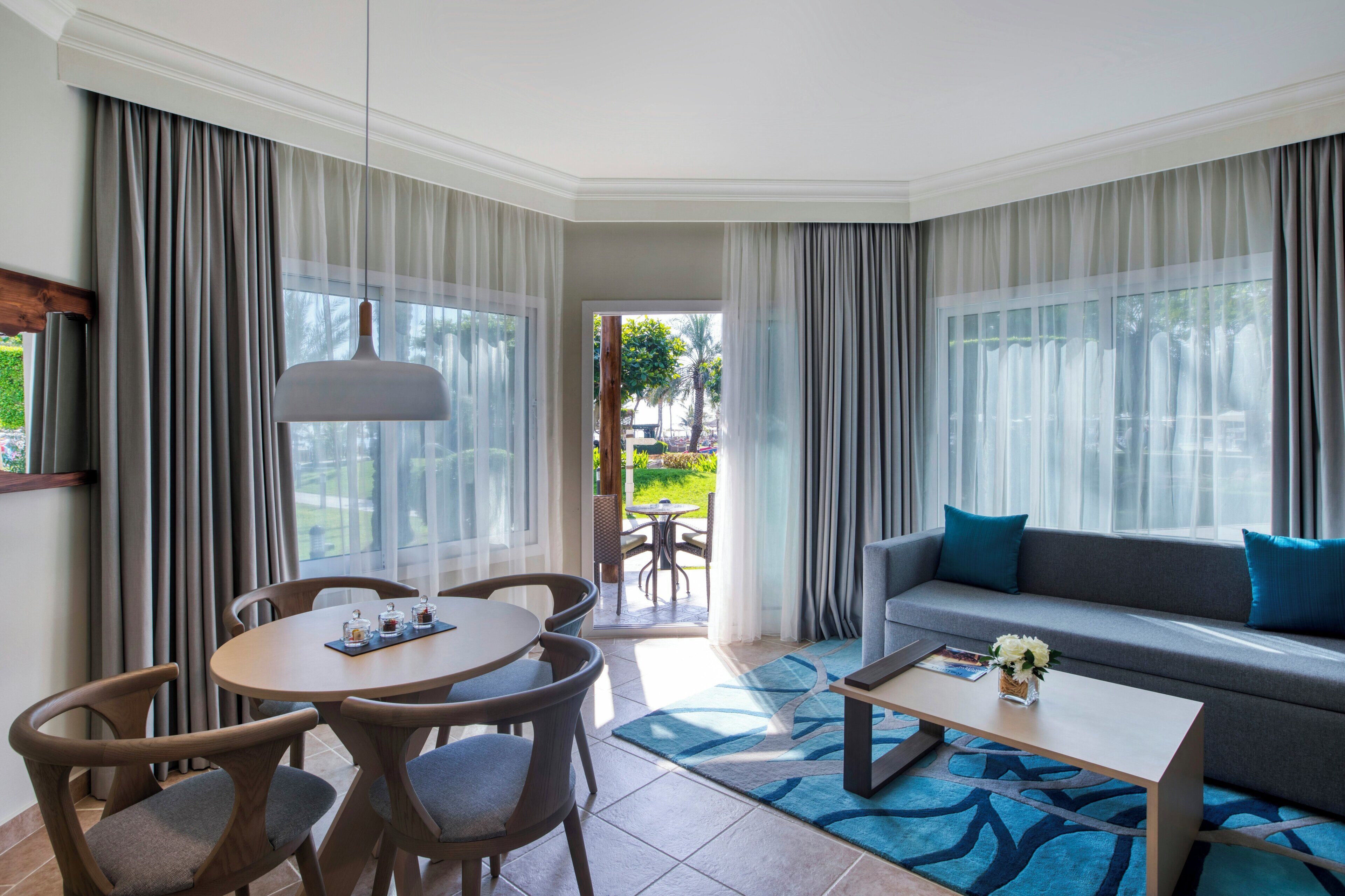 A modern hotel room with a dining area, a sofa, and a view of the outdoors.