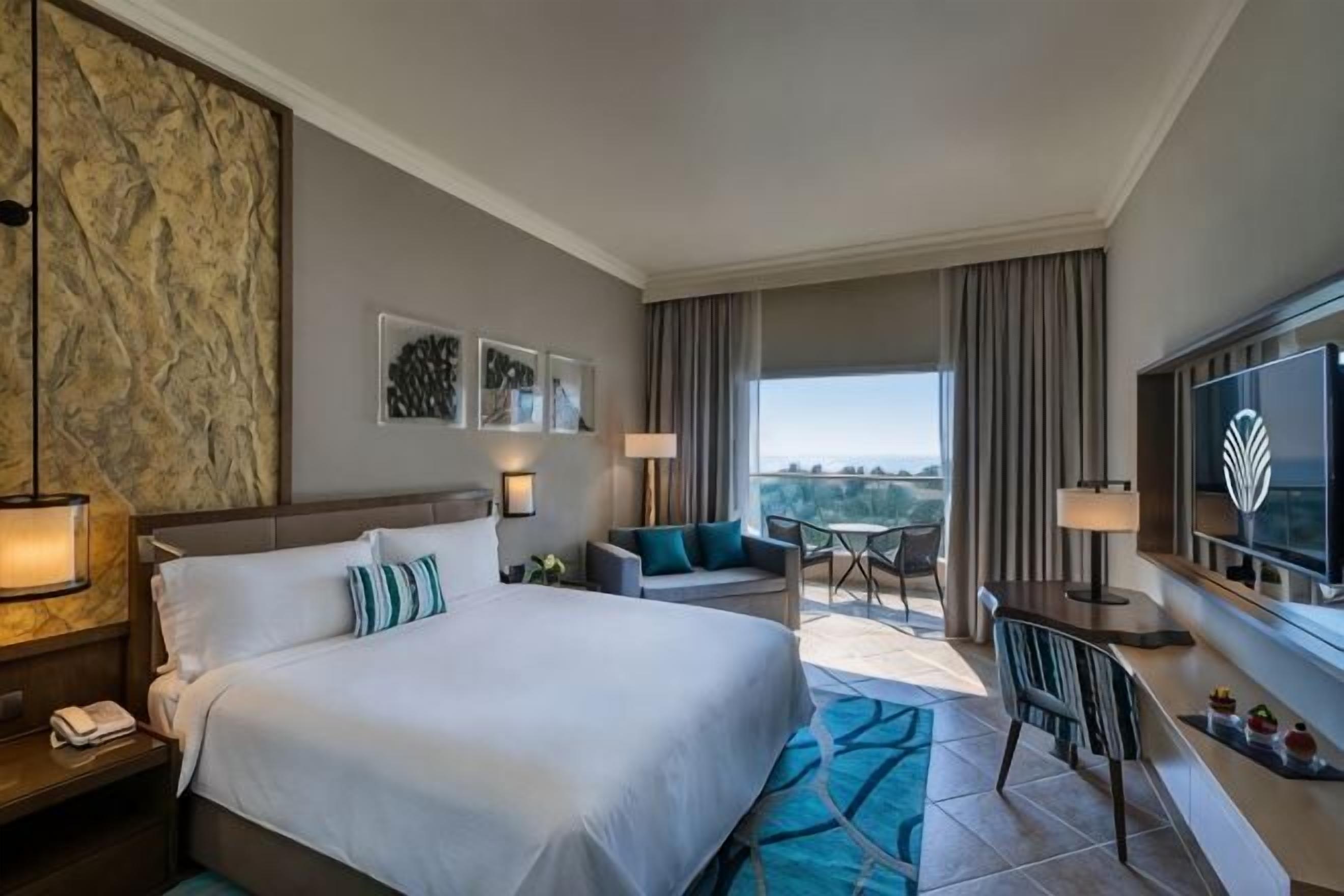 Quarto de hotel com uma cama grande, uma escrivaninha com cadeira, televisão e varanda com vista.