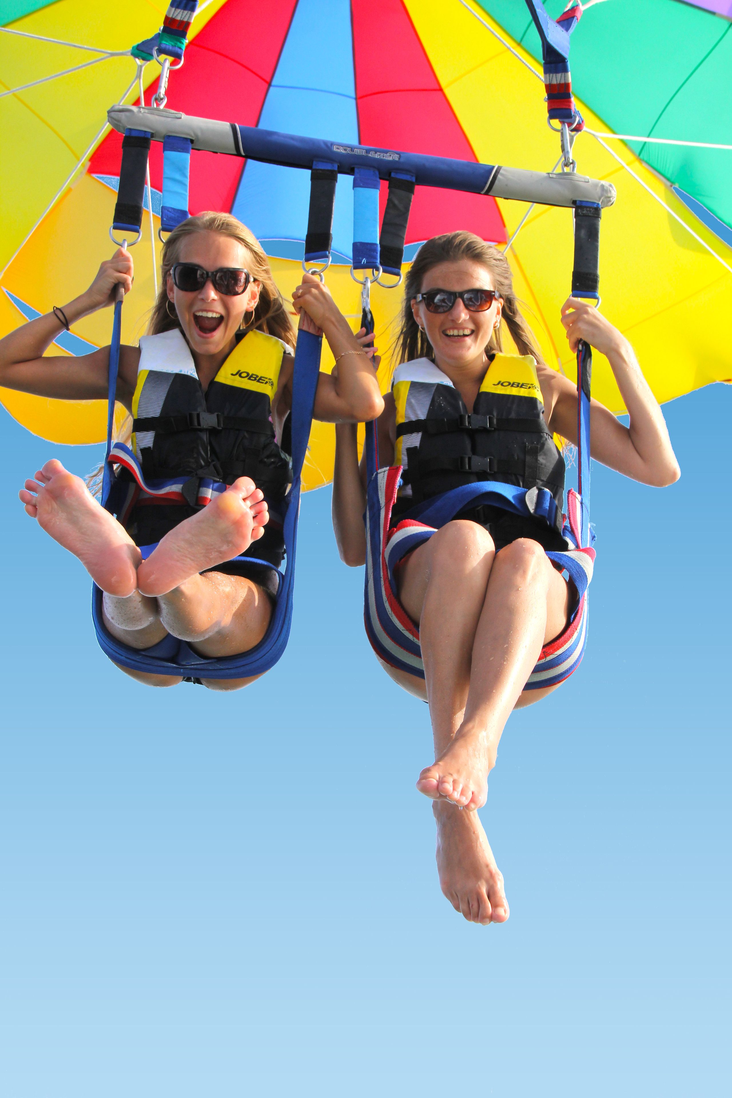 Two people in a tandem chair suspended by a colorful parachute.