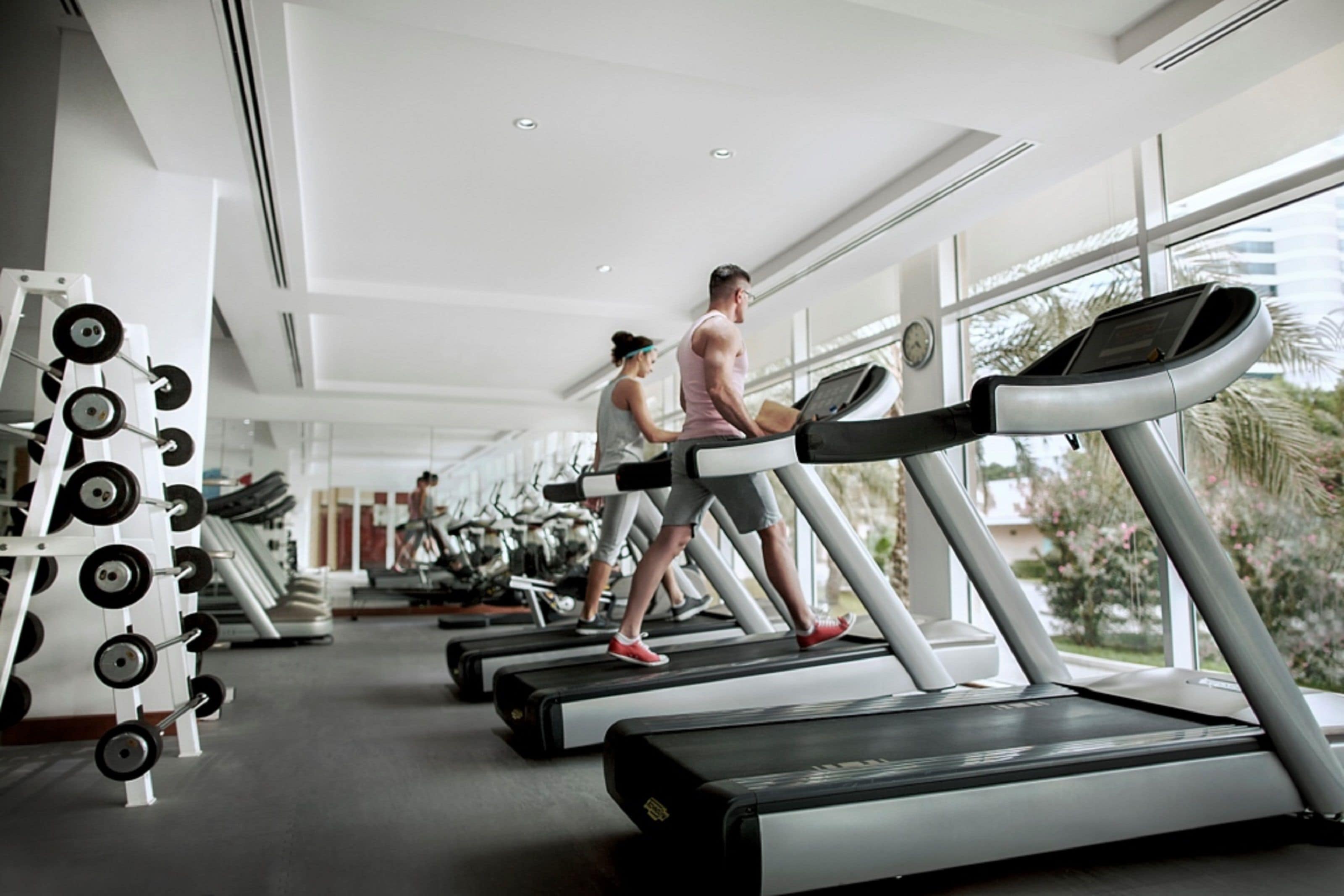 Une salle de sport équipée de tapis de course, d’appareils de musculation et dotée d’une grande fenêtre.
