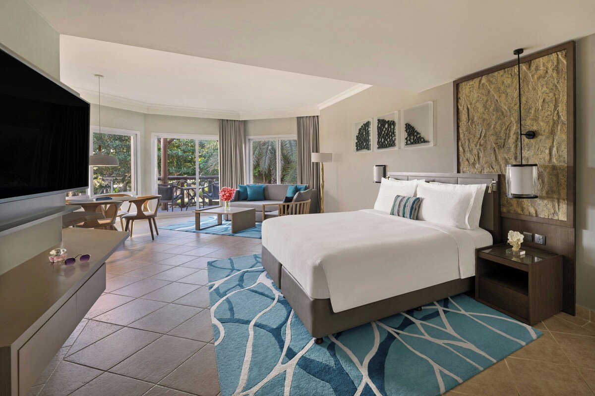 Una habitación de hotel con una cama grande, un escritorio, una silla, un sofá y un balcón con mobiliario exterior.