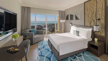 Habitación de hotel con cama, televisor, mesa de comedor y vista a la playa.