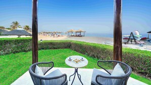 Un patio con sillas de mimbre y una mesa, con vista a una playa con sombrillas y un tobogán de agua.
