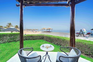 Um pátio com cadeiras de vime e uma mesa, com vista para uma praia com guarda-sóis e um toboágua.