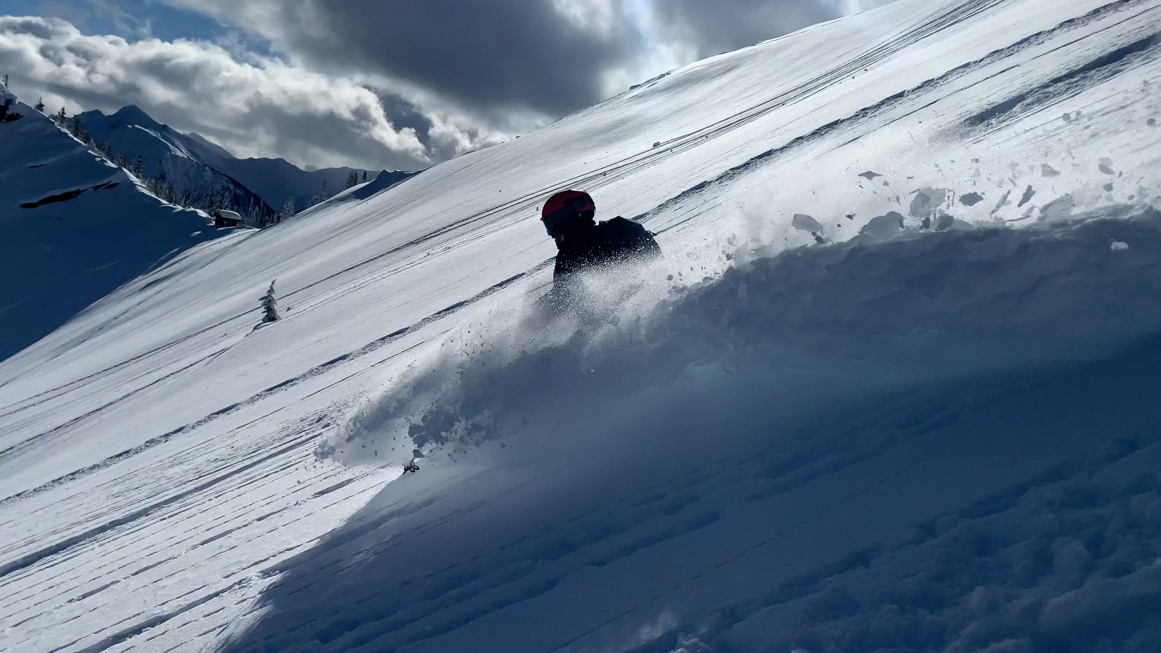 A snowboarder descending a snowy slope with a mountain backdrop.
