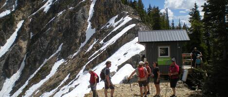 Un groupe de randonneurs se trouve au camp de base d’une montagne, près d’un petit abri et sur des pentes enneigées.