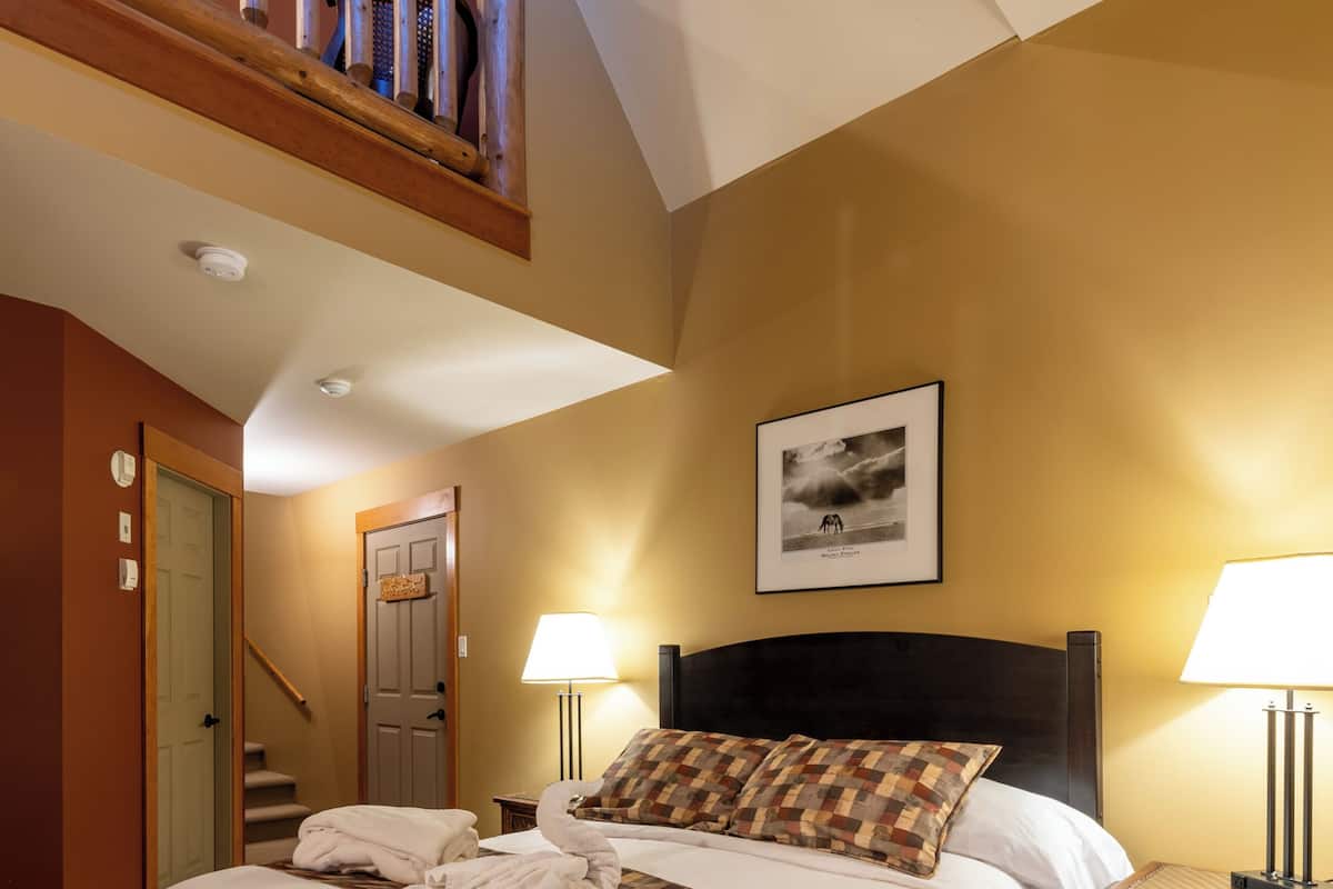 Ein Hotelzimmer mit einem großen Bett, einem Holzkopfschild, einer Treppe und einem gerahmten Bild an der Wand.