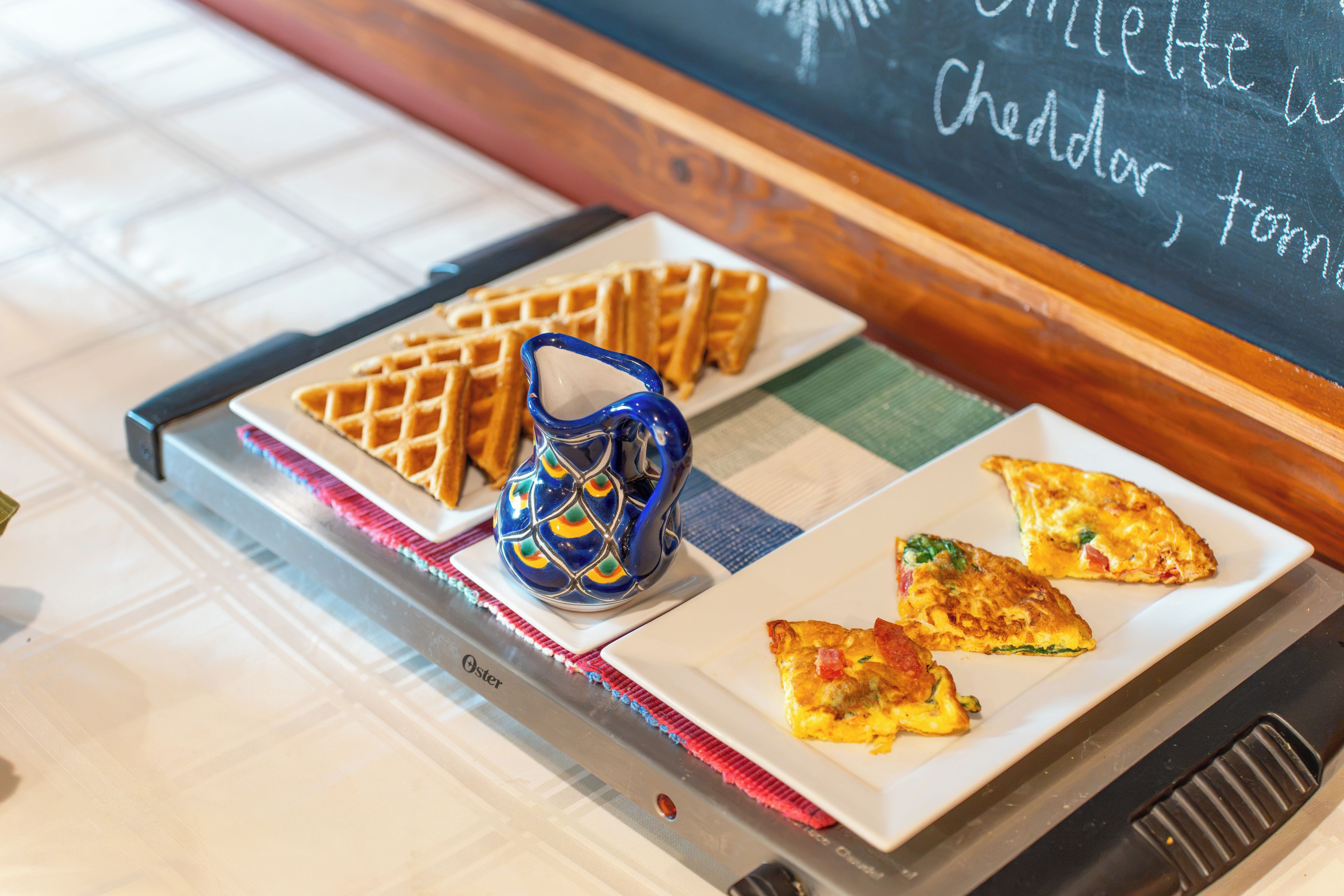 A tray with waffles, a ceramic pitcher, and a plate with omelette slices.