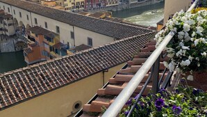 A view of a cityscape with terracotta-tiled rooftops, a river, and buildings with balconies. - Hotel Hermitage (Florence)