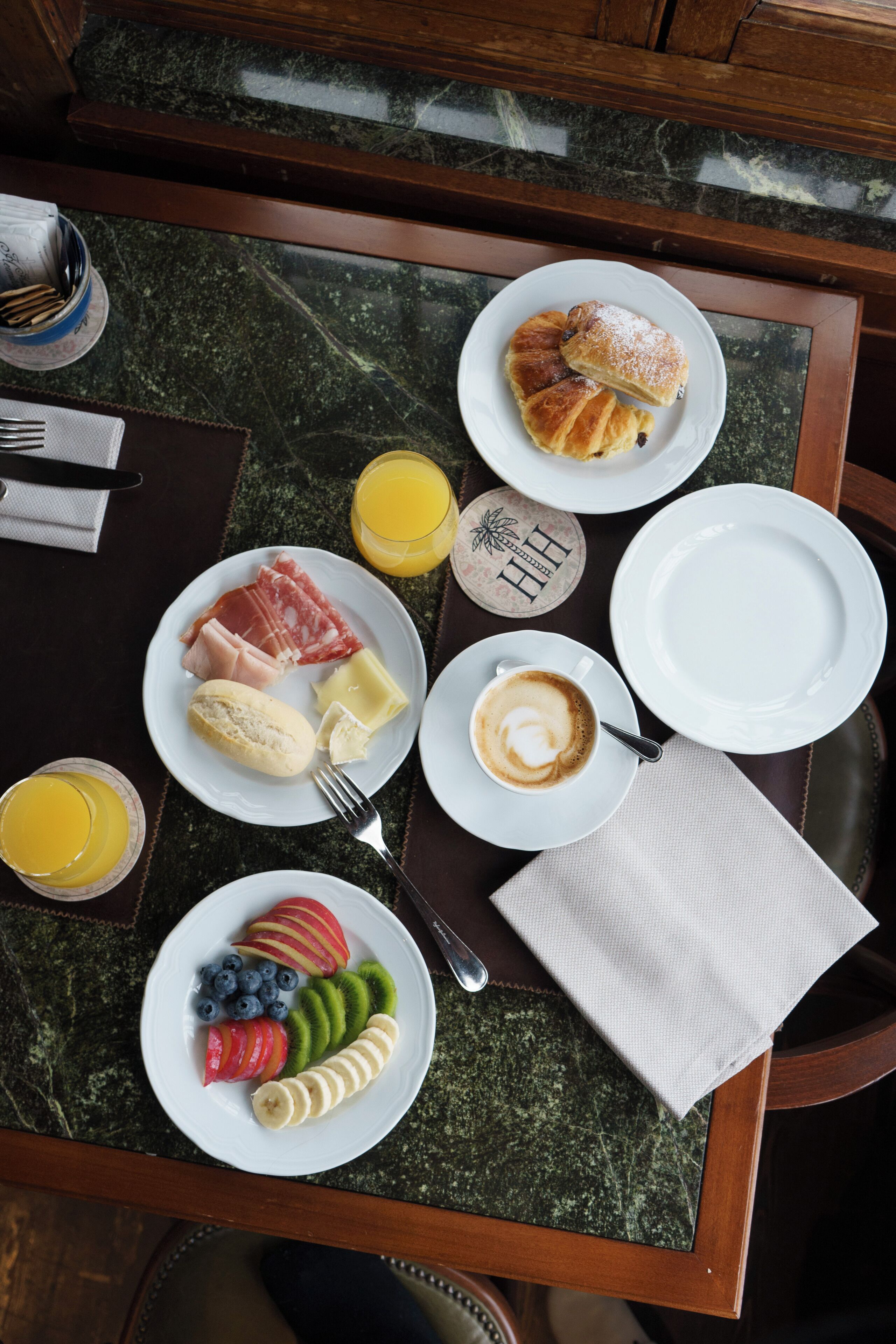 Et morgenbord med tallerkener mad, en kop kaffe og et glas appelsinjuice.