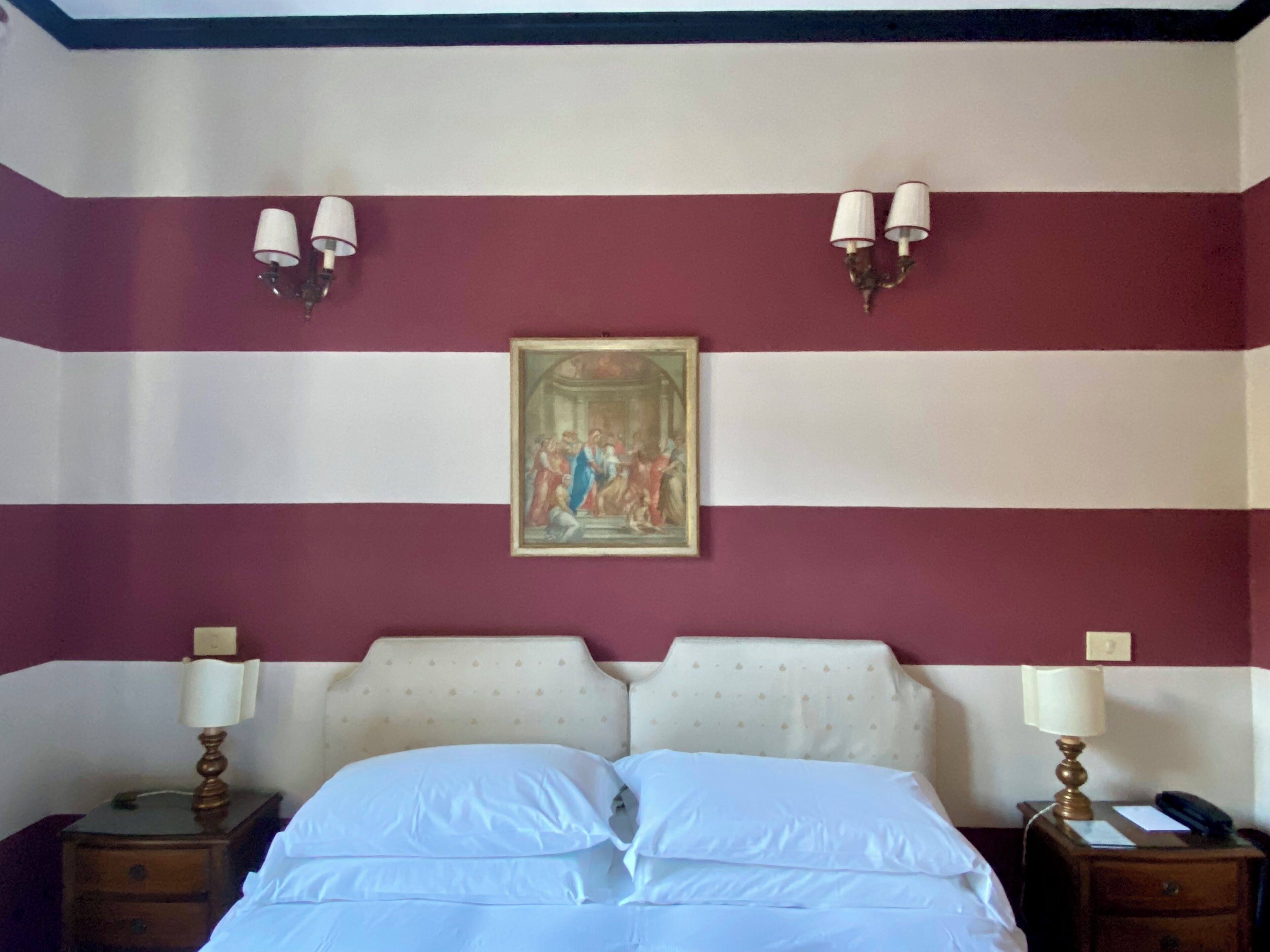Een hotelkamer met een bed, twee bedlampen, een nachtkastje en een schilderij aan de muur.