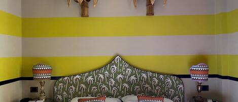 A hotel room with a striped yellow and white wall, a bed with white linens, two decorative wall sconces, and a patterned pillow.