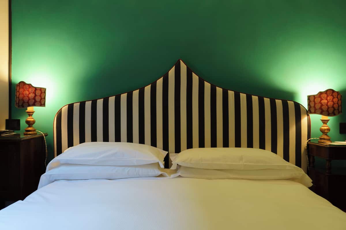 A bed with a striped headboard, white bedding, and two bedside lamps with patterned shades.