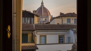 A view through a window of a building with a tiled roof, a dome, and adjacent structures. - Hotel Hermitage (Florence)