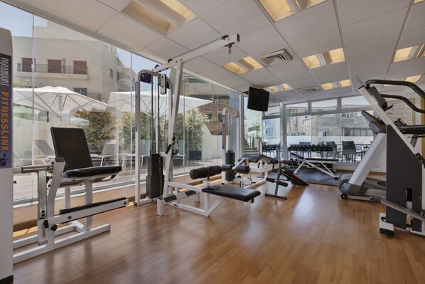 Un gimnasio moderno con diversos equipos de ejercicio, ventanas amplias y vistas a la ciudad.