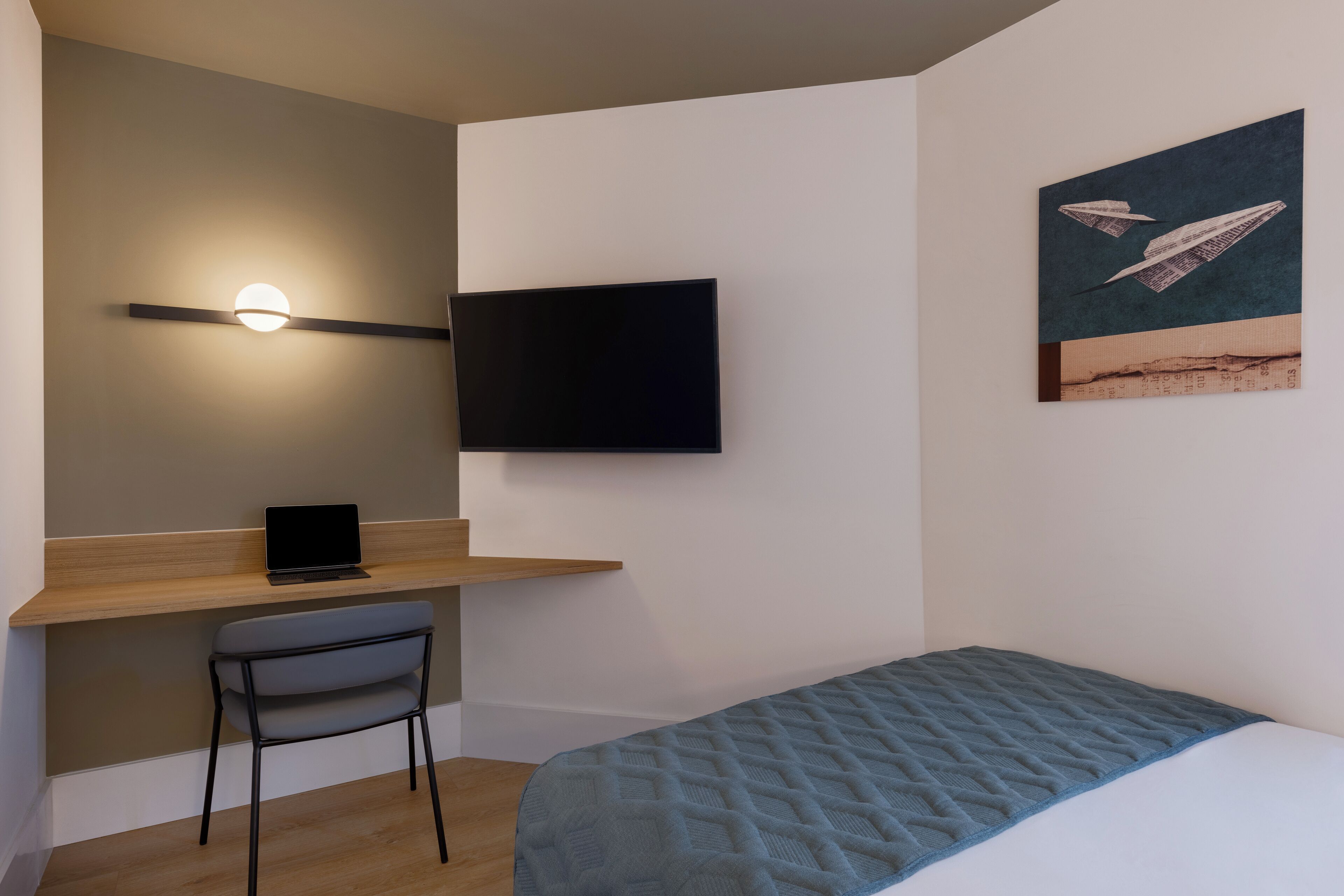 Un dormitorio con cama, escritorio con silla, televisor de pantalla plana y estante fijado a la pared.