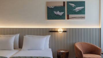 A hotel room with a bed, pillows, a round wooden side table, a chair, and wall art depicting paper airplanes.
