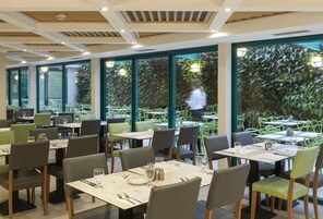 Comedor interior con mesas y sillas, ventanas amplias y vistas a zonas verdes exteriores.