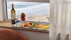 Una mesa con una botella de vino, dos copas y una variedad de frutas y frutos secos, cerca de una ventana con vistas a la playa.