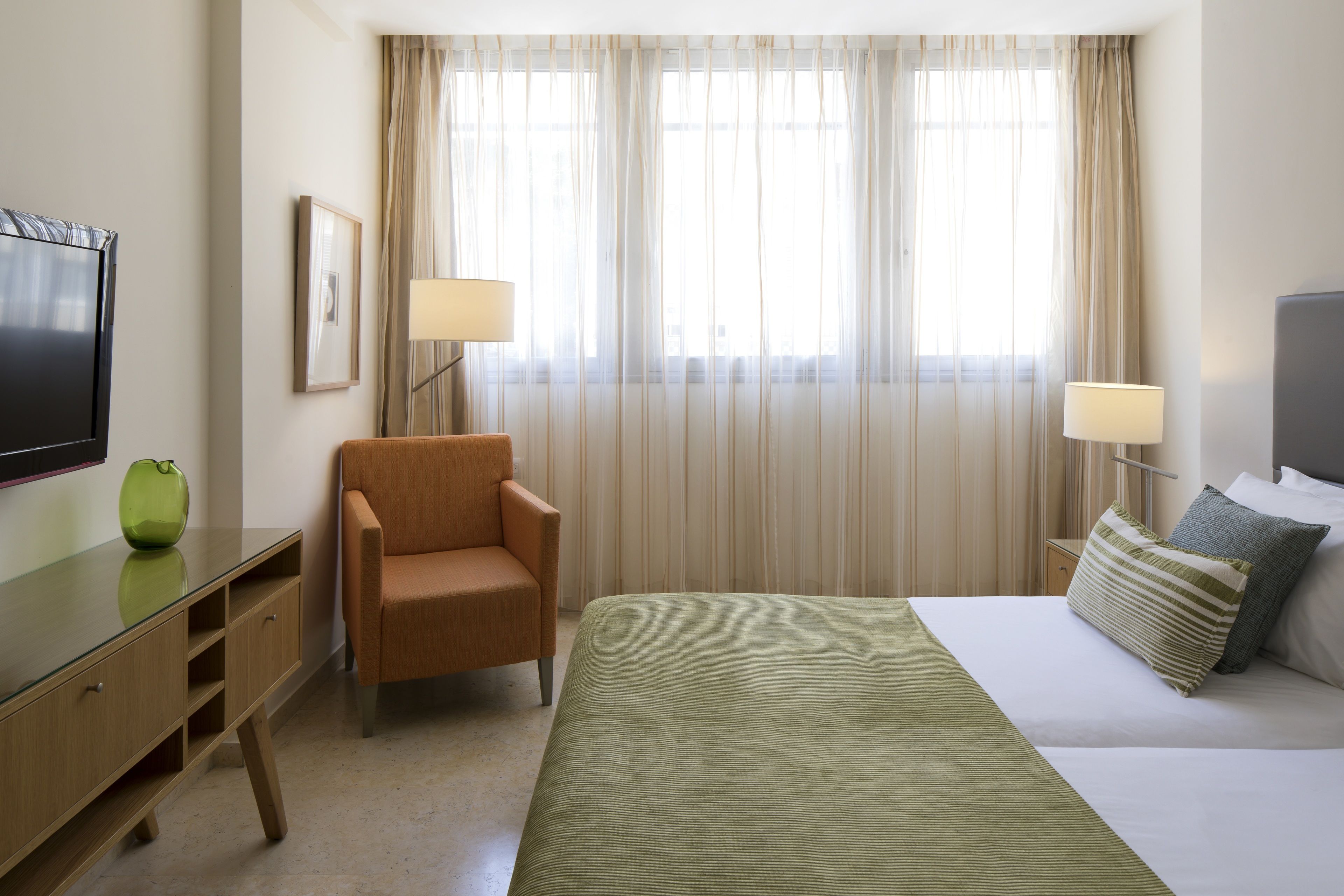 Una camera d'albergo con un letto, una scrivania, una sedia, una televisione e una finestra con tende.