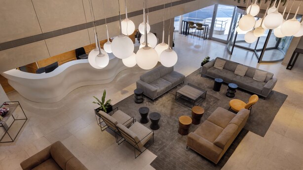 Un vestíbulo amplio con un mostrador de recepción curvo, varias zonas de estar con sofás y sillones, e iluminación colgante con lámparas esféricas.