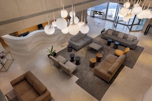 Un vestíbulo amplio con un mostrador de recepción curvo, varias zonas de estar con sofás y sillones, e iluminación colgante con lámparas esféricas.